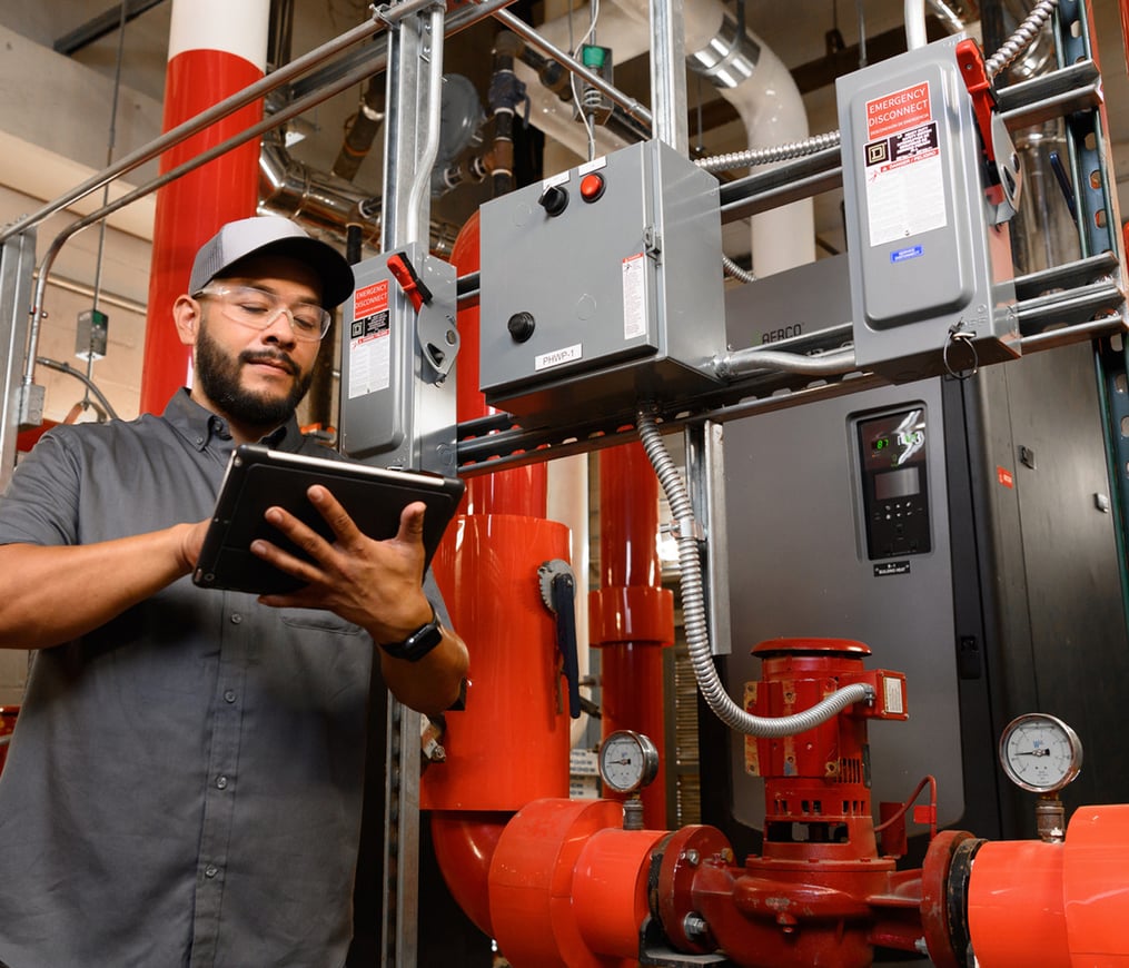 Commercial HVAC technician checks system performance using an iPad with shiny, red equipment in the background